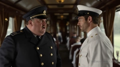 In the dining car of a historic train. An older, corpulent man is standing on the left. He is wearing a blue uniform with a double row of buttons and an officer&rsquo;s cap. On the right is a young man in a white uniform with a white officer&rsquo;s cap. The older man is scolding the younger man. The younger man looks away, embarrassed.