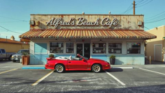 Ein etwas heruntergekommenes Strandcafé in San Francisco: Die Fassade ist dreckig, die Farbe blättert ab, und die Markise ist verdreckt. Ein roter Firebird parkt vor dem Eingang.