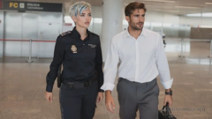 In der Empfangshalle eines Flughafens. Links: Miray in der Uniform einer spanischen Inspectora. Rechts: Dian in einem weißen Hemd und einer grauen Hose, der einen schwarzen Lederkoffer trägt. Sie blicken in die Ferne, als hätten sie jemanden entdeckt.
