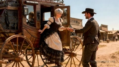 Eine Stagecoach steht auf der staubigen Hauptstraße eines Örtchens im Wilden Westen. Ein Kutscher steht an der Tür und hilft Miray beim Aussteigen. Sie trägt einen eleganten Petticoat in hellen und dunklen Farben. (KI-generiertes Bild)